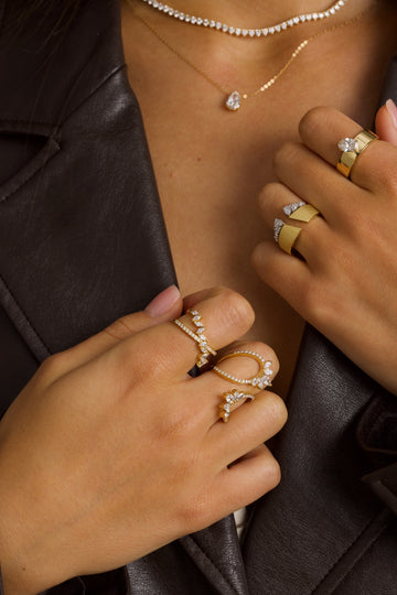 Close-up of hands wearing multiple gold and diamond rings on a dark background