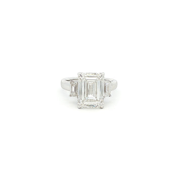 Three-stone ring featuring a lab-grown emerald cut center diamond with two emerald side stones, set in a classic design with 18k gold