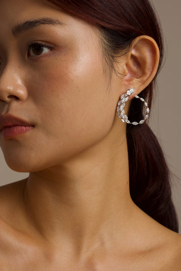 Close-up of a woman wearing a white gold serpent hoop earring against a neutral background