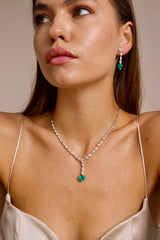 A woman wearing an emerald necklace and earrings with a neutral background