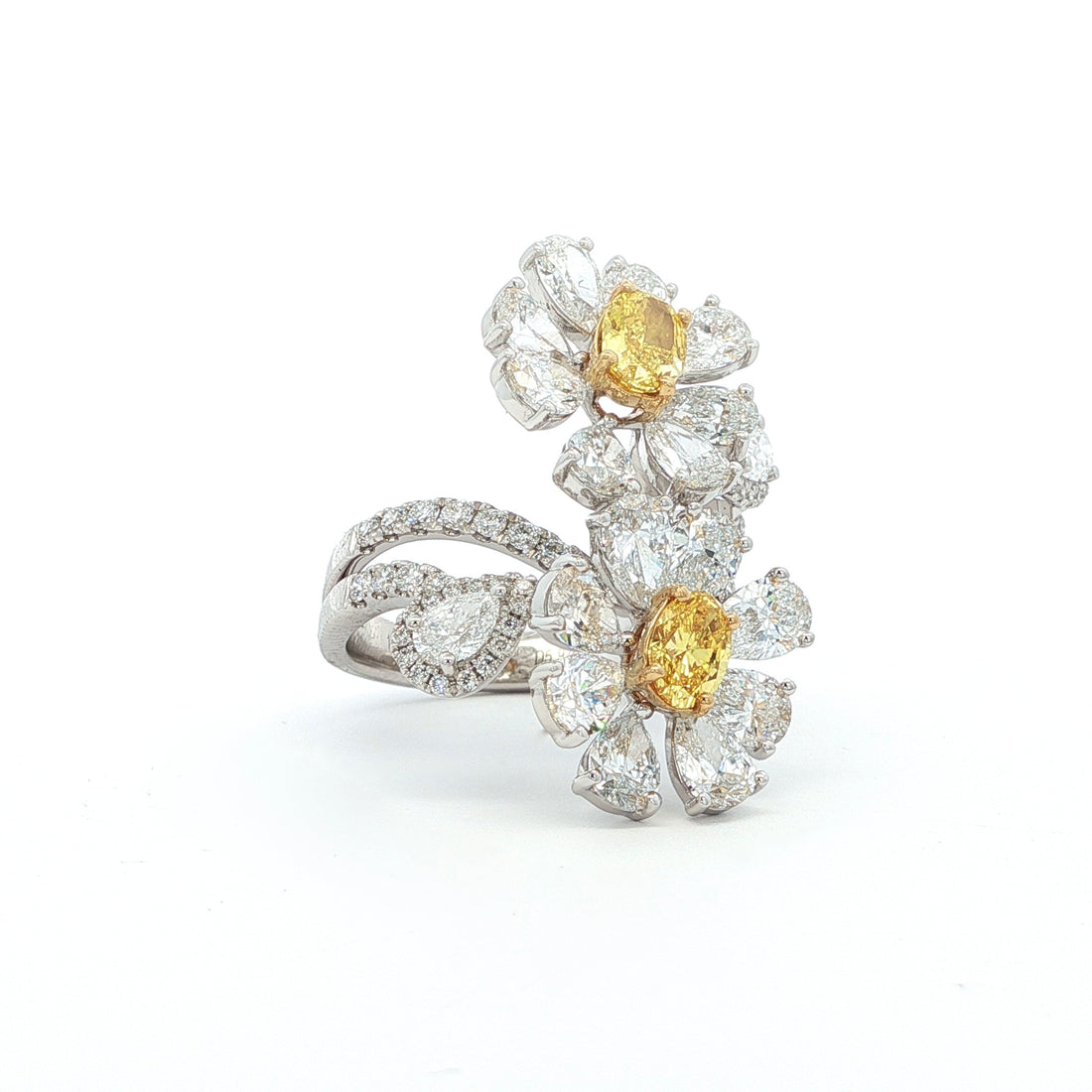 This 18K White Gold ring features a floral-inspired design with two oval-cut fancy yellow diamonds, expertly cut in a brilliant style. These radiant gems are accented by white diamond "petals"; creating a stunning contrast and adding to the ring's overall charm and opulence. A true statement piece for any special occasion!