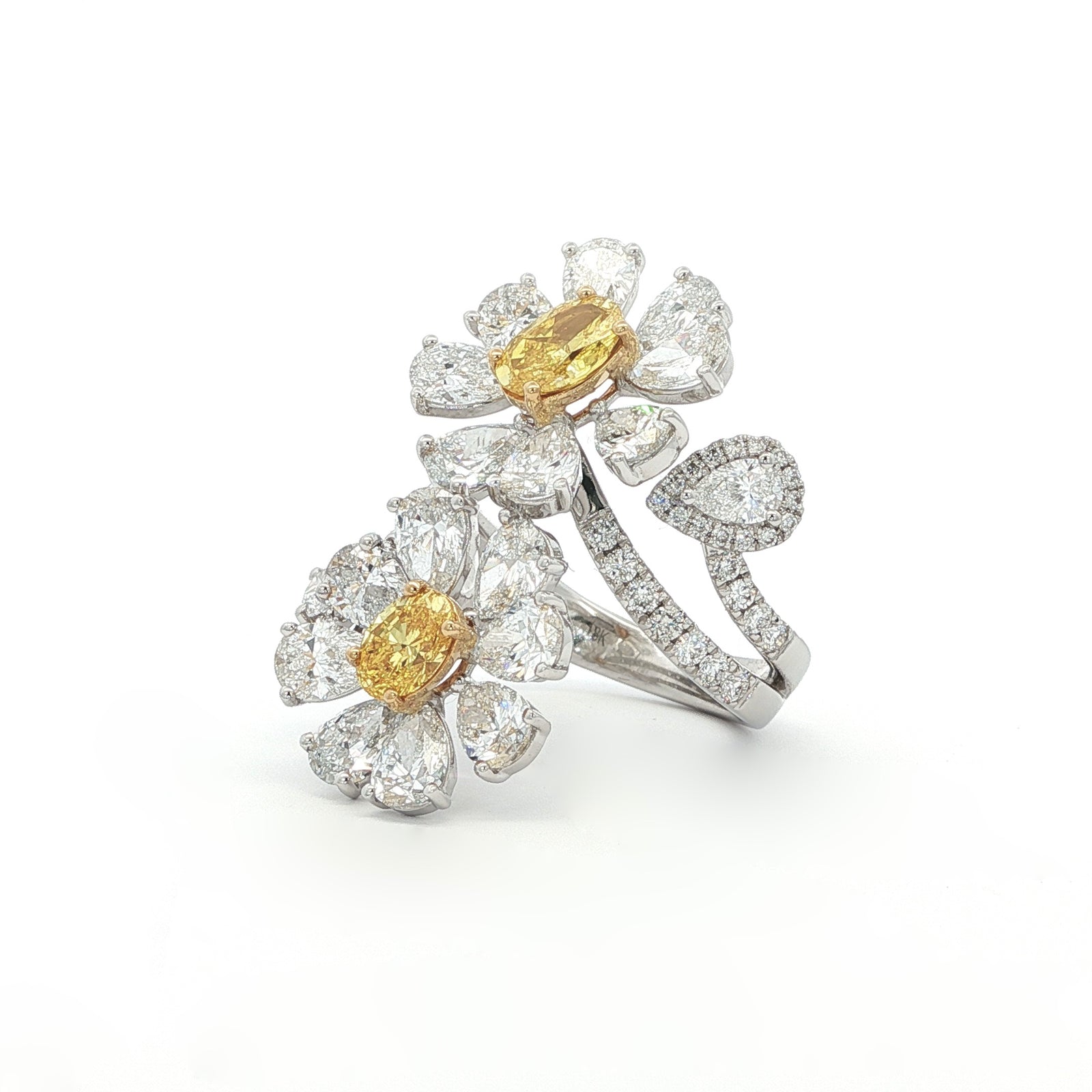 This 18K White Gold ring features a floral-inspired design with two oval-cut fancy yellow diamonds, expertly cut in a brilliant style. These radiant gems are accented by white diamond "petals"; creating a stunning contrast and adding to the ring's overall charm and opulence. A true statement piece for any special occasion!