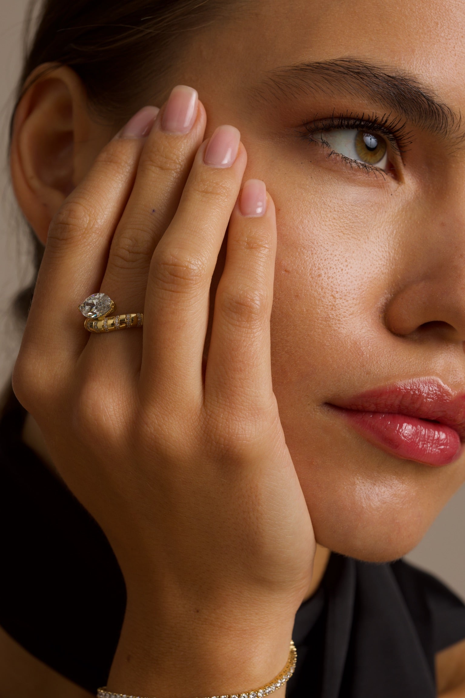 Close-up of a woman's face with a hand touching her cheek, wearing a gold ring.