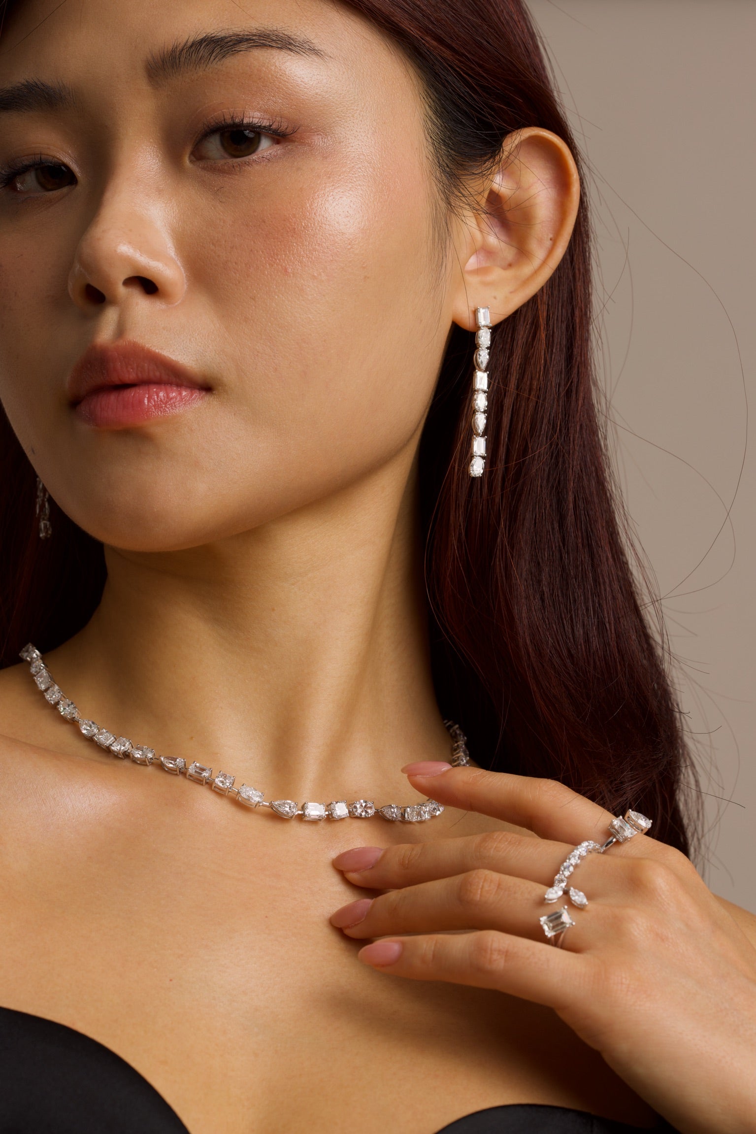 Woman wearing a diamond necklace, drop earrings, and ring against a neutral background