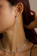 Close-up of a person wearing a diamond necklace and drop earrings.
