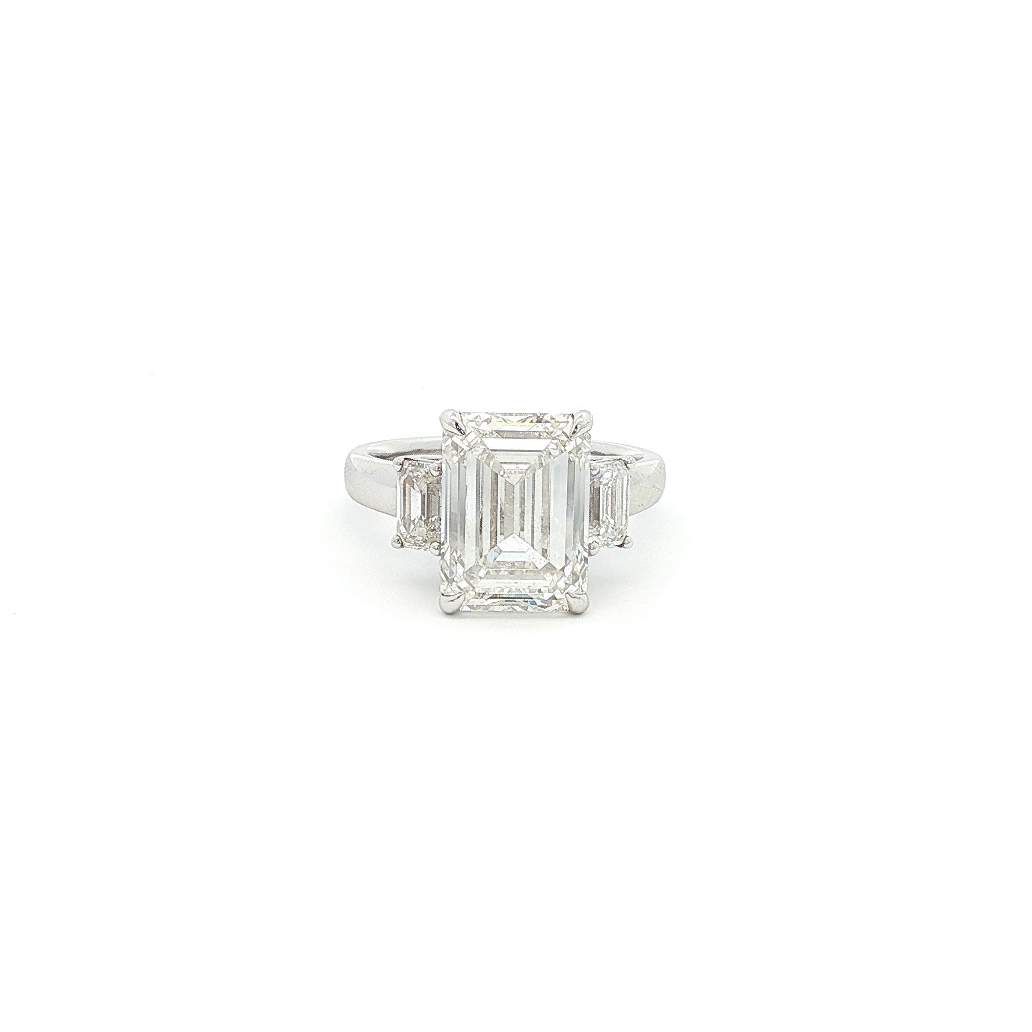 Three-stone ring featuring a lab-grown emerald cut center diamond with two emerald side stones, set in a classic design with 18k gold