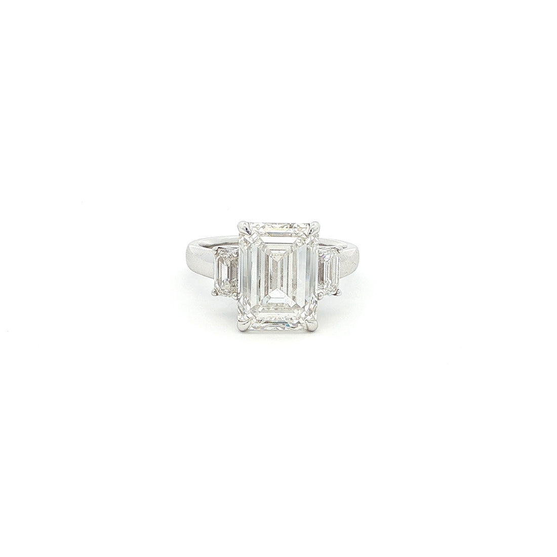Three-stone ring featuring a lab-grown emerald cut center diamond with two emerald side stones, set in a classic design with 18k gold