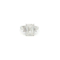 Three-stone ring featuring a lab-grown emerald cut center diamond with two emerald side stones, set in a classic design with 18k gold