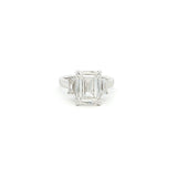 Three-stone ring featuring a lab-grown emerald cut center diamond with two emerald side stones, set in a classic design with 18k gold