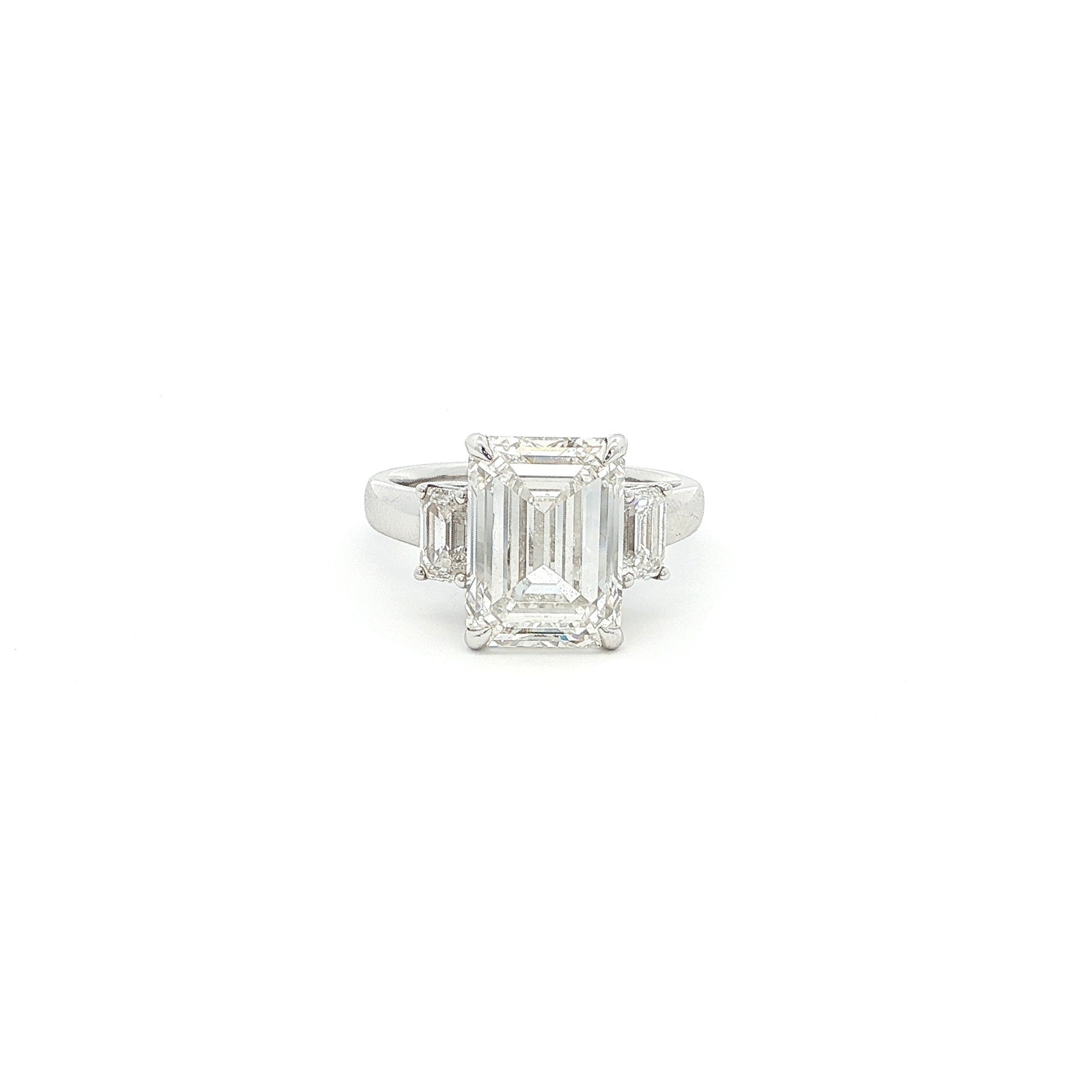 Three-stone ring featuring a lab-grown emerald cut center diamond with two emerald side stones, set in a classic design with 18k gold