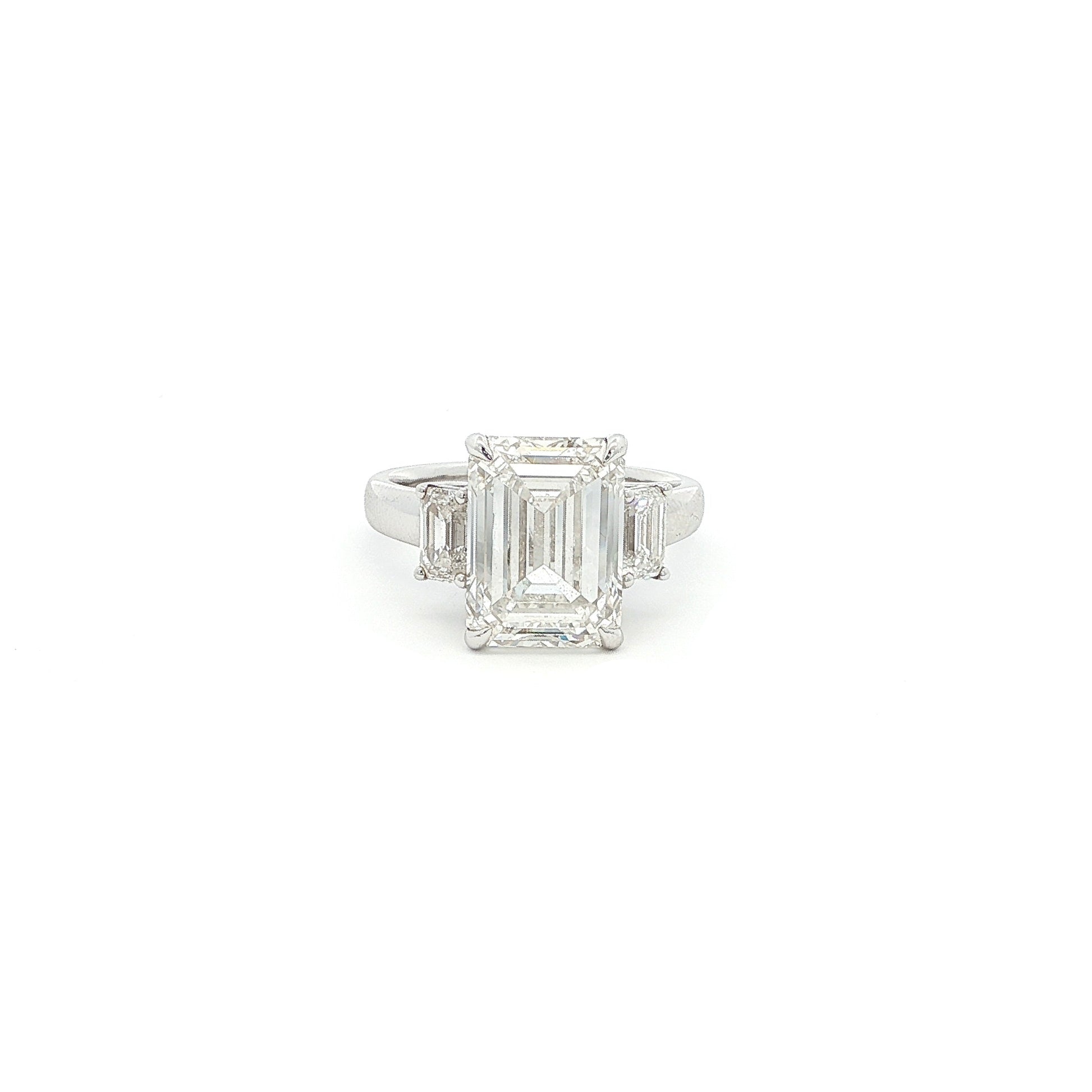 Three-stone ring featuring a lab-grown emerald cut center diamond with two emerald side stones, set in a classic design with 18k gold