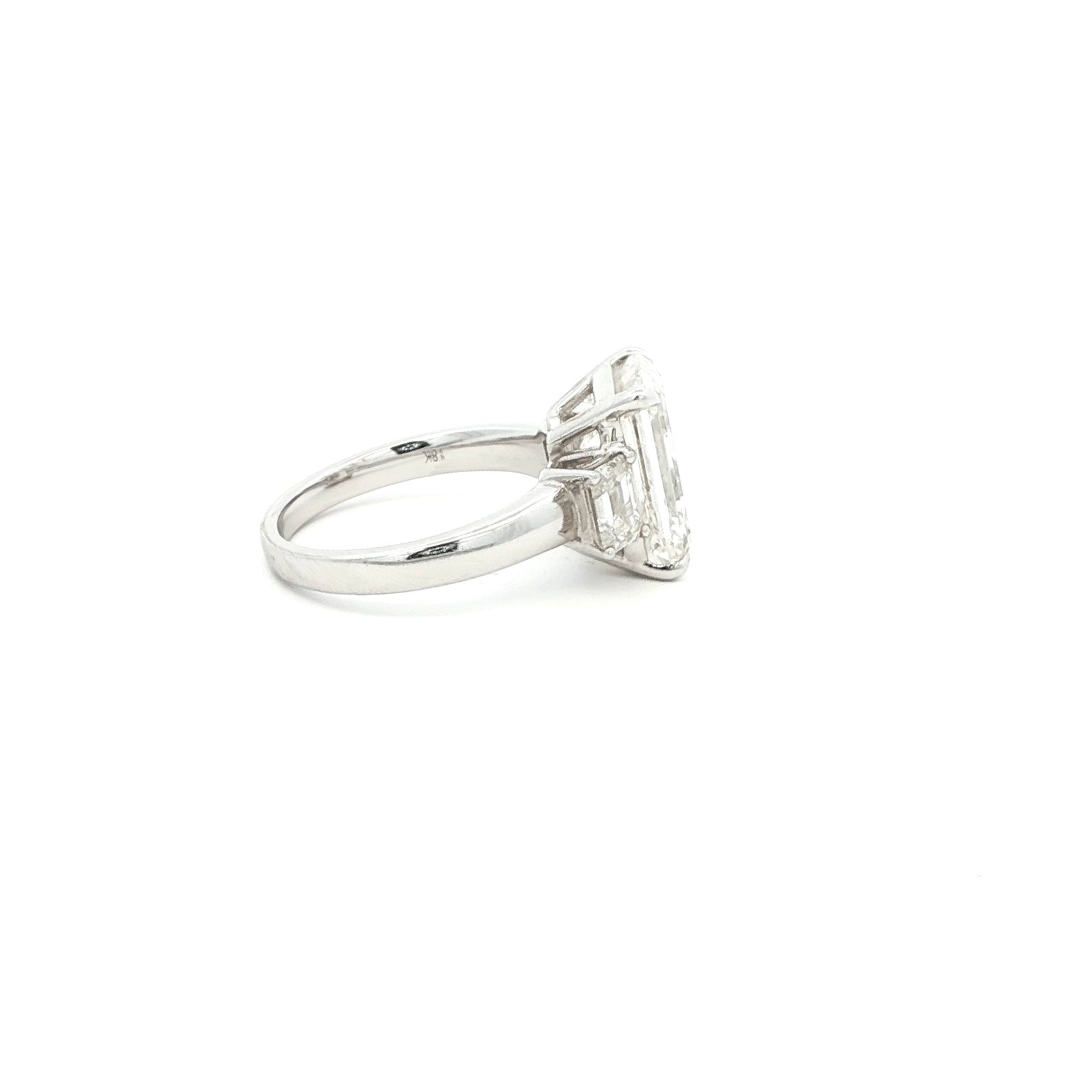 Three-stone ring featuring a lab-grown emerald cut center diamond with two emerald side stones, set in a classic design in 18k gold.