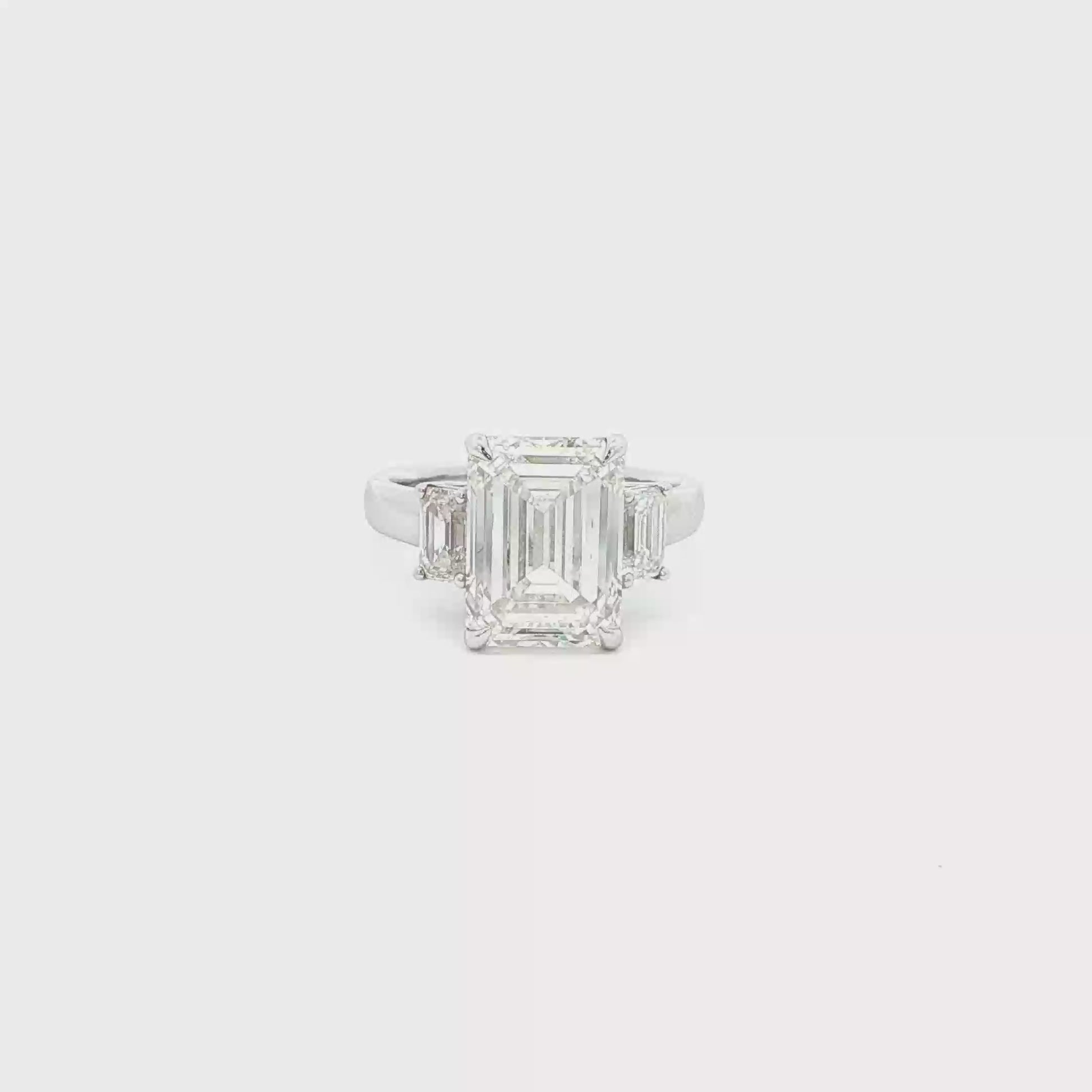 Three-stone ring featuring a lab-grown emerald cut center diamond with two emerald side stones, set in a classic design.